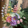 A handmade crochet flower bouquet featuring various shades of pink, yellow, and purple flowers.