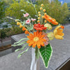 Handmade crochet flower bouquet featuring orange, yellow, and pink blooms on green stems