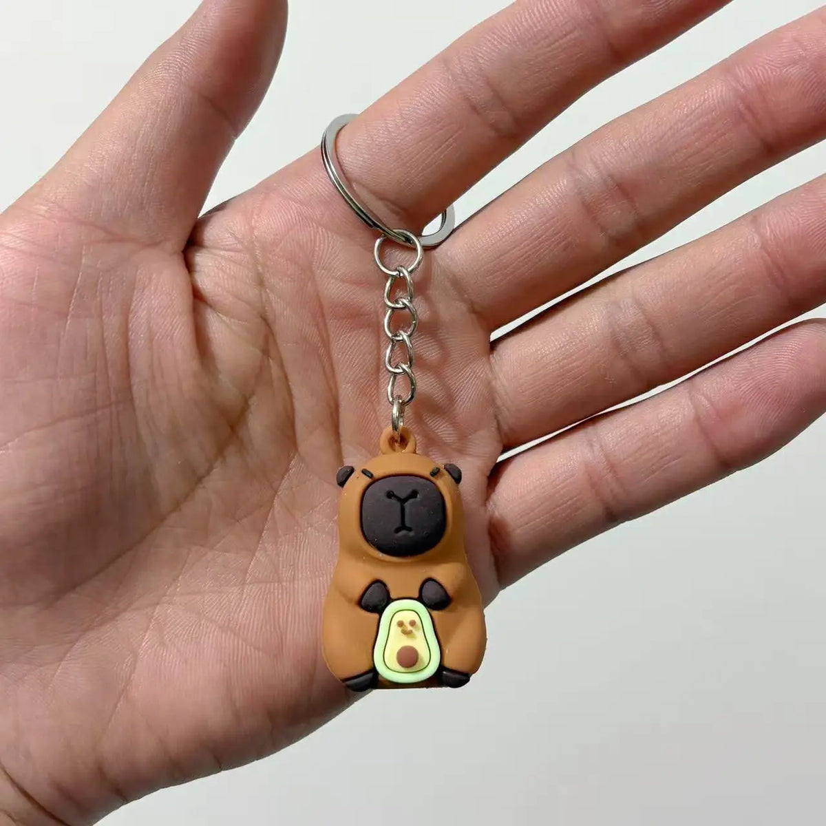 Un petit pendentif de capybara brun rond sur une chaîne en argent tenu dans la main d'une personne.