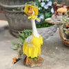 A ceramic goose figurine wearing a yellow polka-dot costume, placed outdoors on a stone surface.