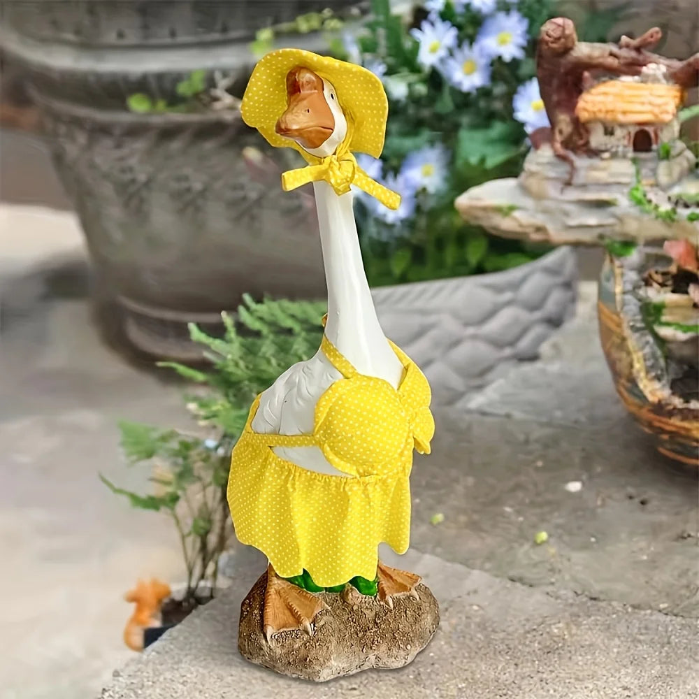 A ceramic goose figurine wearing a yellow polka-dot costume, placed outdoors on a stone surface.