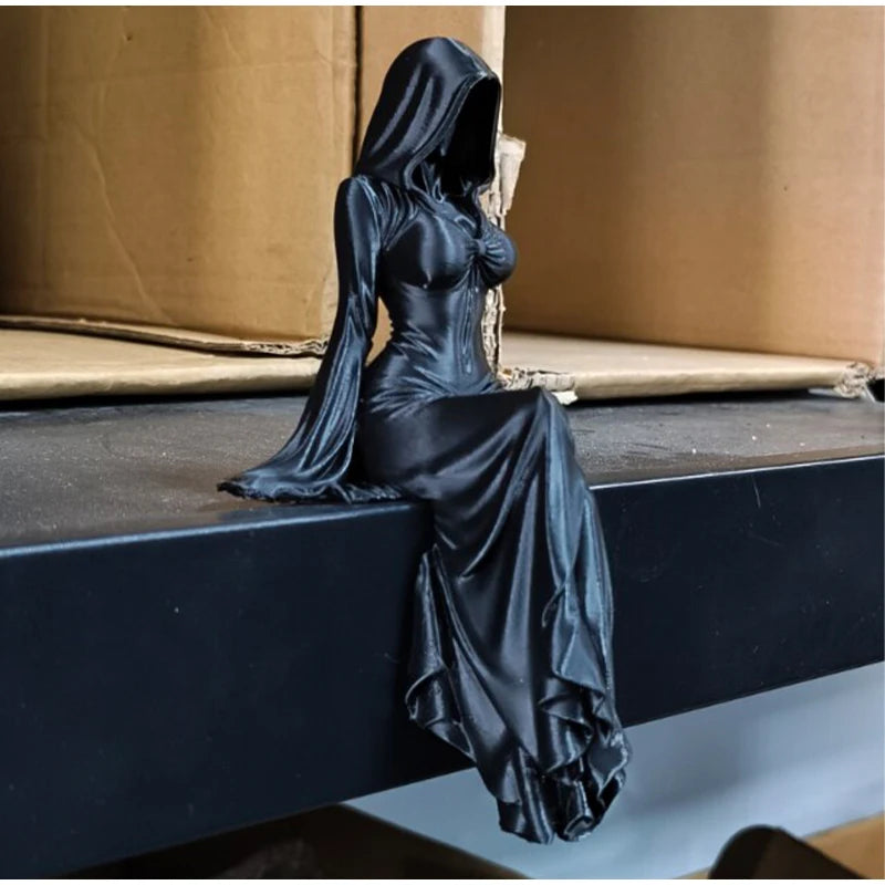 A black figurine of a woman in a hooded gown sitting on a dark surface.