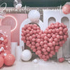 A heart shape made of pink latex balloons surrounded by white balloons and a light pink background.