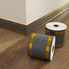 Rolls of self-adhesive PVC skirting board trim in gray and gold accents resting on a wooden floor.