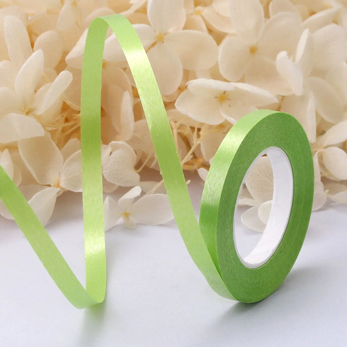 A green satin balloon ribbon roll shaped like the infinity symbol is displayed against a background of light cream flowers.