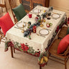A white rectangle tablecloth decorated with a Christmas theme featuring poinsettia leaves and greenery set for a meal.