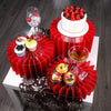 A red folding dessert table display featuring cupcakes and a tiered cake on a white stand.