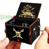 A carved wooden music box with a lid featuring a pirate theme and a small key.