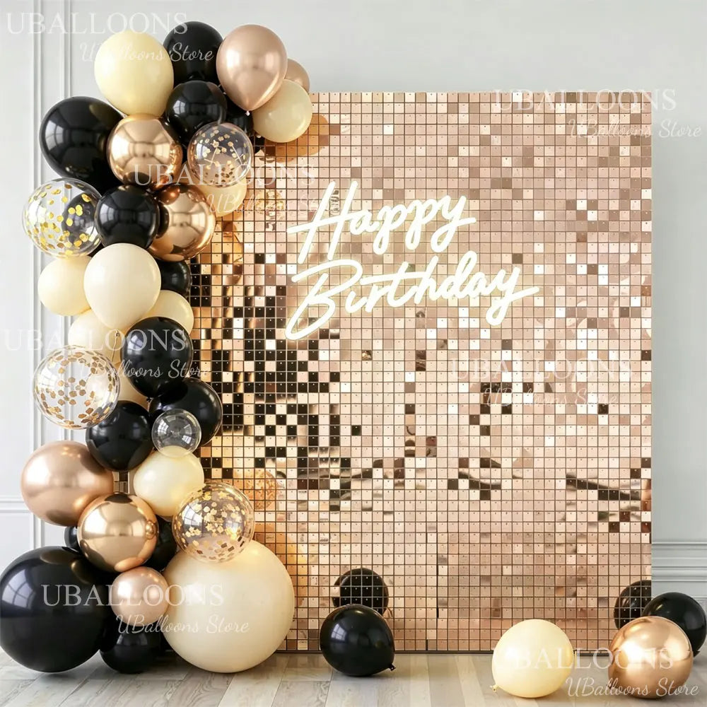 A gold and black balloon arrangement against a square wall backdrop with happy birthday text.