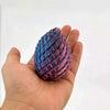 A hand holds a textured, purple and blue dragon egg fidget toy with a scale pattern.
