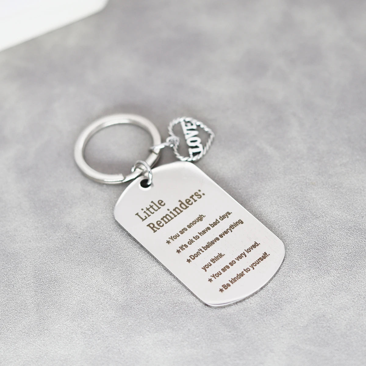A silver heart-shaped stainless steel keychain with engraved inspirational reminders on a gray background.