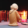 A small, smooth, tan resin figurine of a monk in robes is lit by a nearby candle.