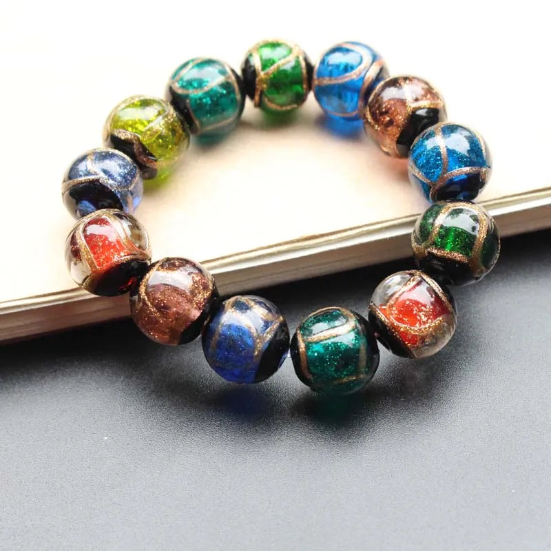 A bracelet made of handcrafted lampwork glass beads featuring various iridescent colors including blue, green, and gold accen