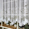 White lace mesh sheer curtain hanging in a rod pocket, featuring floral patterns.