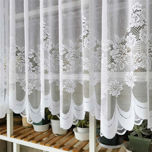 White lace mesh sheer curtain hanging in a rod pocket, featuring floral patterns.
