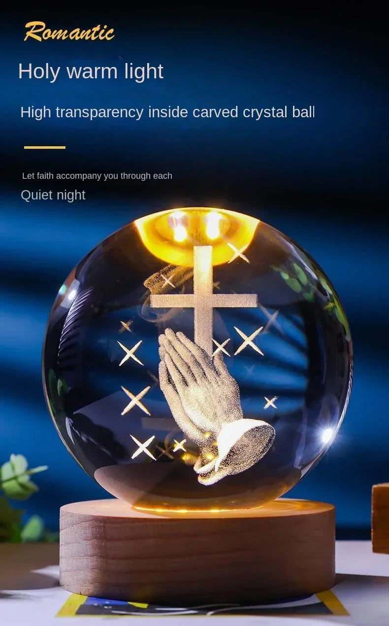 A clear glass crystal ball night light featuring a golden warm light illuminating a hand and a cross.