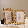 A pair of ornate golden resin photo frames featuring delicate fern designs on a light pink background.