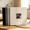 A linen front scrapbook memory book with a light beige cover and a dark spine, resting on a wooden surface.