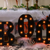 Un letrero de marquesina negro con forma de 'BOO' y luces naranjas brillantes sobre una mesa.