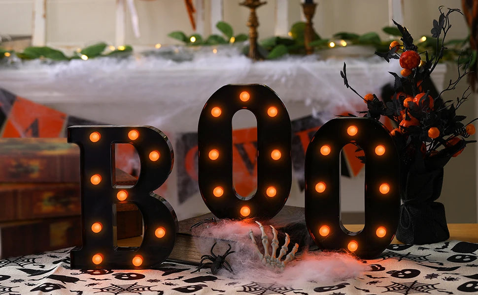 Un letrero de marquesina negro con forma de 'BOO' y luces naranjas brillantes sobre una mesa.