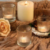 A collection of vintage stripe glass votive candle holders and a lit pillar candle resting on brown fabric.