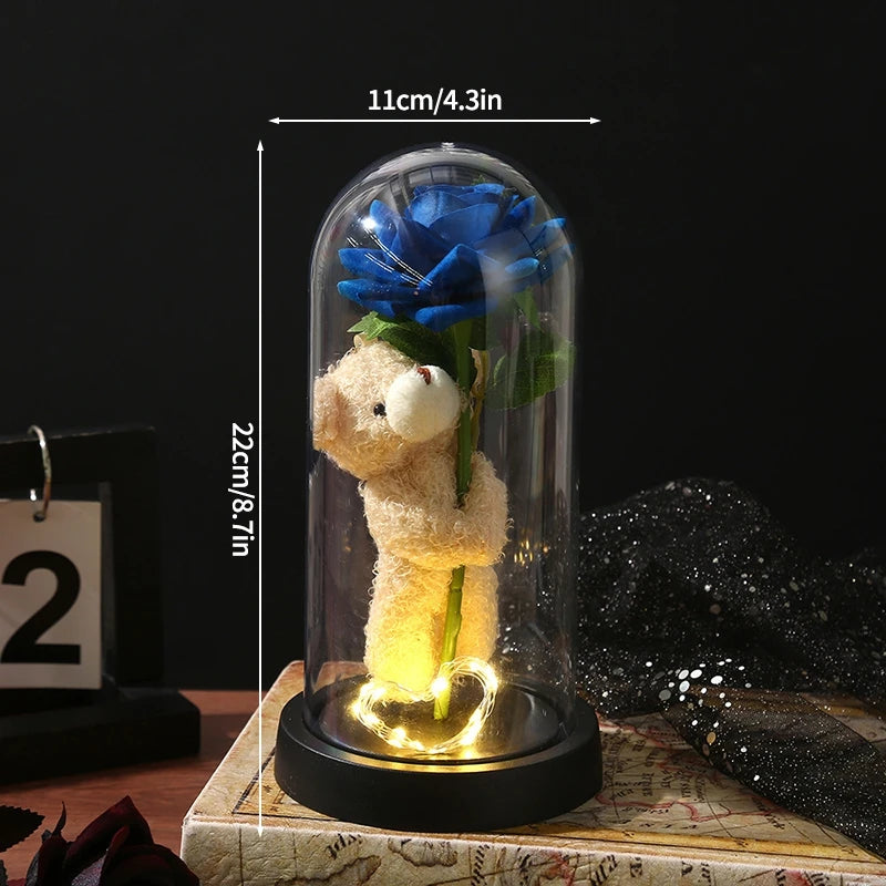 A glass dome display featuring a teddy bear made of yellow material and an eternal blue rose.