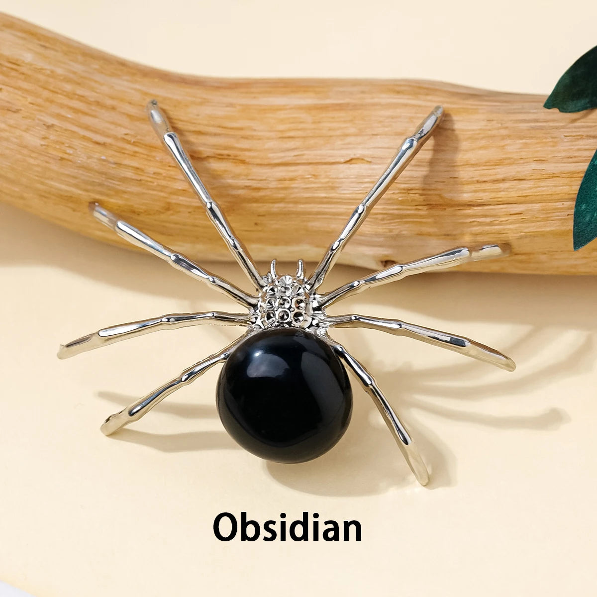 A handcrafted crystal spider figurine with silver legs and a black obsidian body resting on a wooden surface.