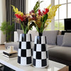 A minimalist black and white checkered ceramic vase displayed on a white table in a living room setting.