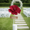 A red velvet peony flower is placed on a white sign marking a wedding ceremony aisle.