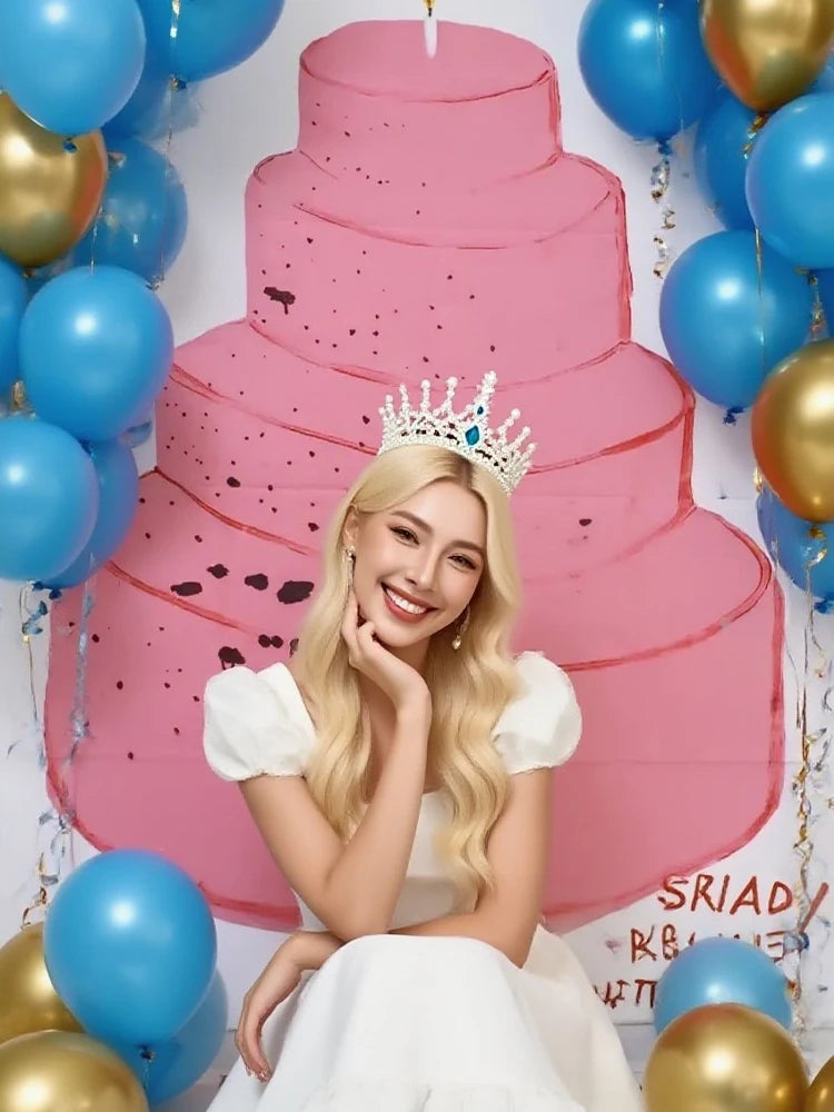 A blonde woman in a white dress poses in front of a multi-tiered pink cake backdrop decorated with gold and blue balloons.