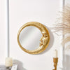A round gold resin decorative hanging mirror with a crescent moon shape mounted on a white wall.