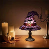 A purple witch hat night light with a stained glass effect sits on a wooden table next to several candles and autumn leaves.