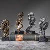 A set of three resin figurines depicting faces in various states of emotion and texture, displayed on a surface.