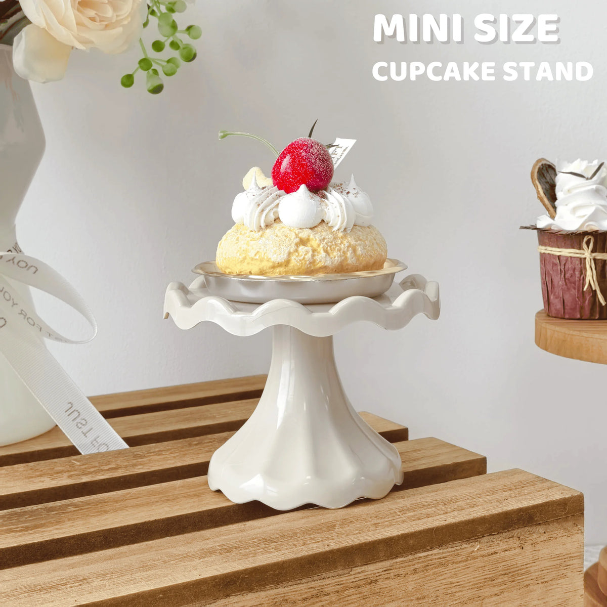 A mini size cupcake stand displaying a single decorated cupcake with white frosting and a red berry on a wooden surface.