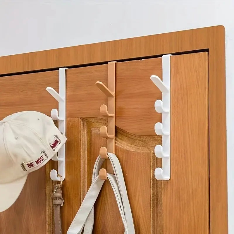 A wooden door with white over-the-door hooks installed for hanging bags, hats, and scarves.