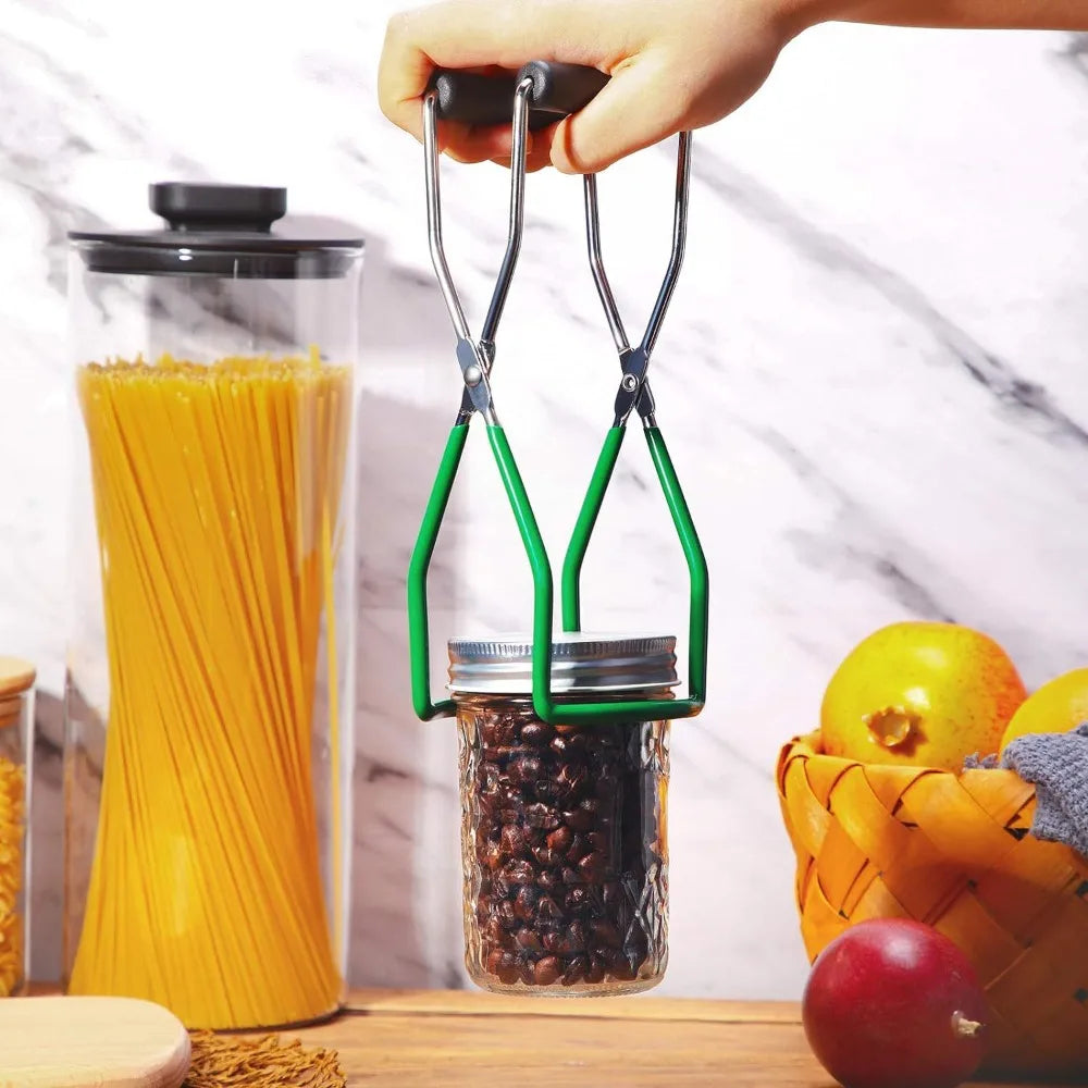 A hand is using a stainless steel canning jar lifter with a non-slip grip to lift a glass jar filled with coffee beans.
