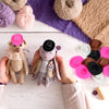 Une paire de mains tient une peluche cowgirl et plusieurs petits cadeaux western sur une surface en bois blanc.