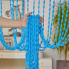 A hand is pulling a bright blue beaded string curtain with tassels, used as a bohemian drape.