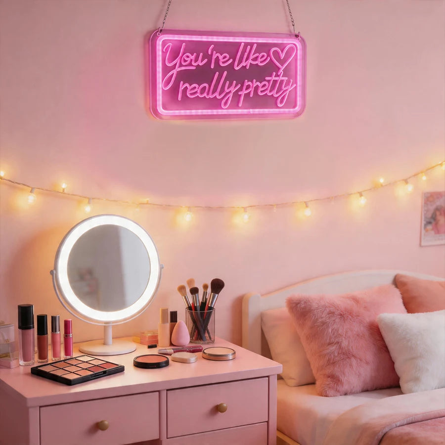 A pink neon sign that reads You're like really pretty hangs above a mirror and string lights in a bedroom setting.