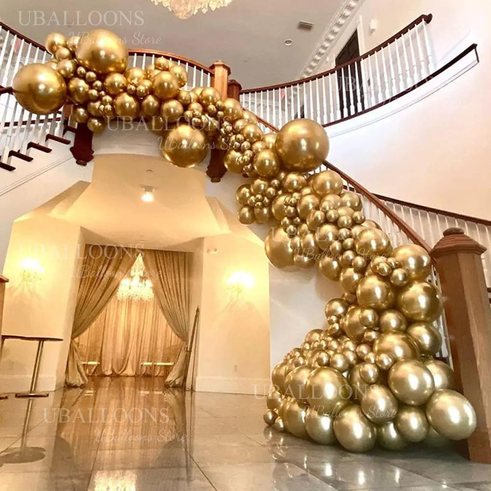 A golden metallic balloon garland decorates a staircase railing in an indoor setting.