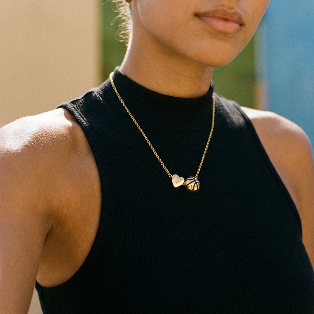 A close-up of a woman wearing a gold heart basketball pendant necklace on a black turtleneck top.
