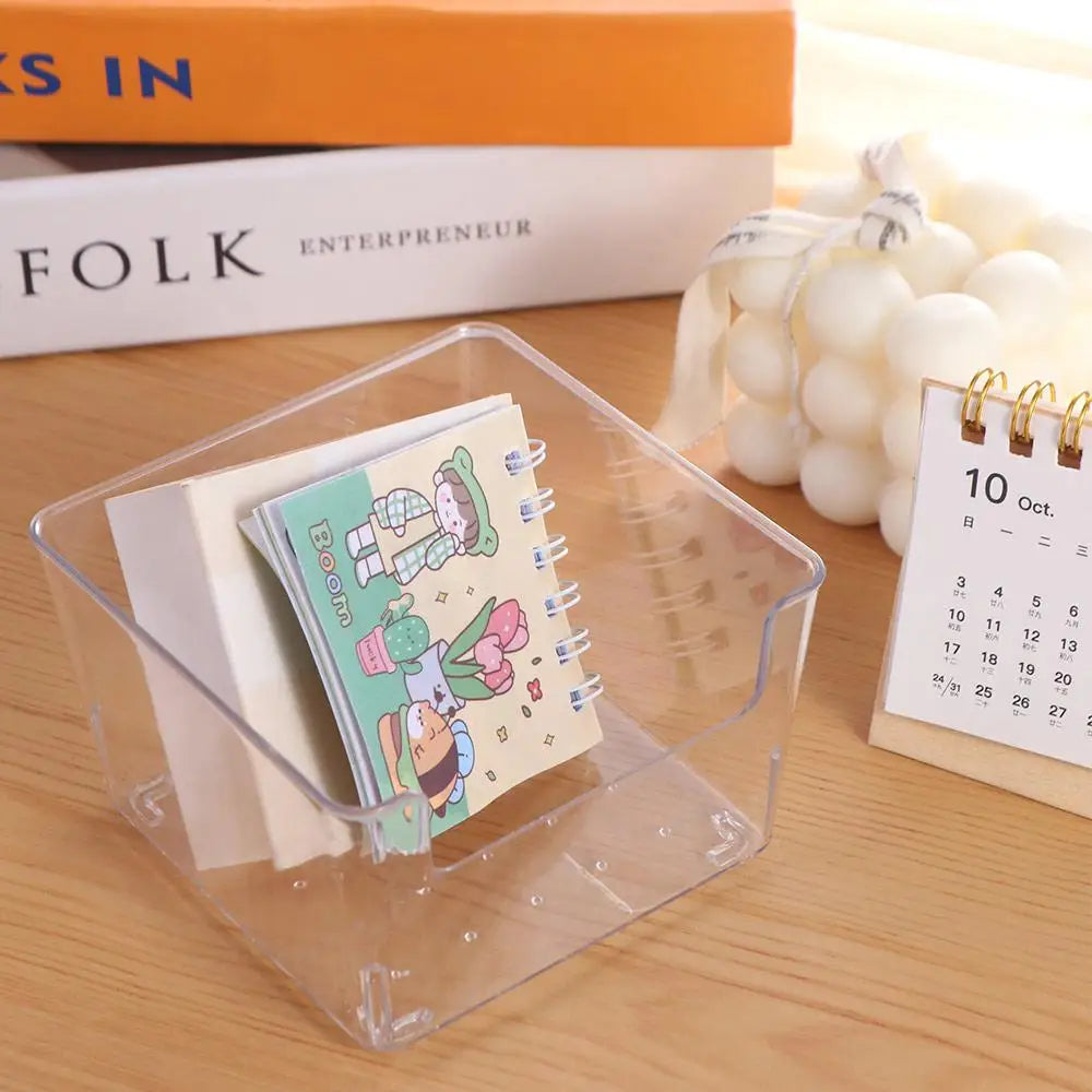 Une boîte d'organisation de bureau en acrylique transparent contient un carnet et plusieurs livres sur une surface en bois.