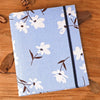 A light blue linen photo album featuring a white floral pattern and black trim, resting on a wooden surface.