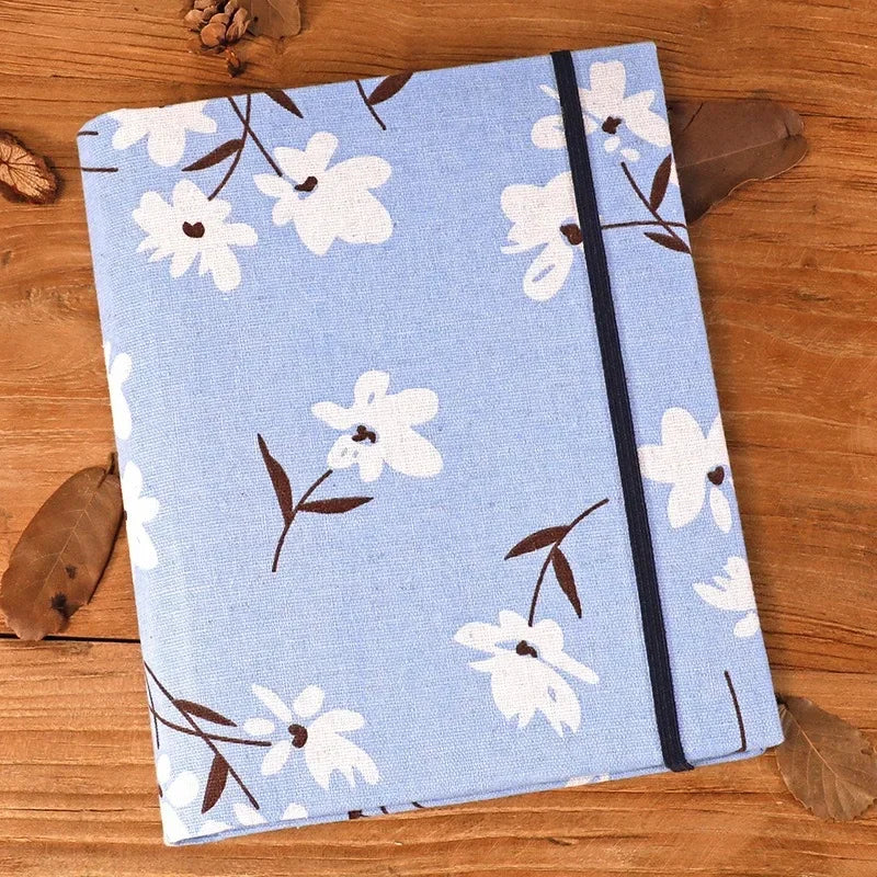 A light blue linen photo album featuring a white floral pattern and black trim, resting on a wooden surface.