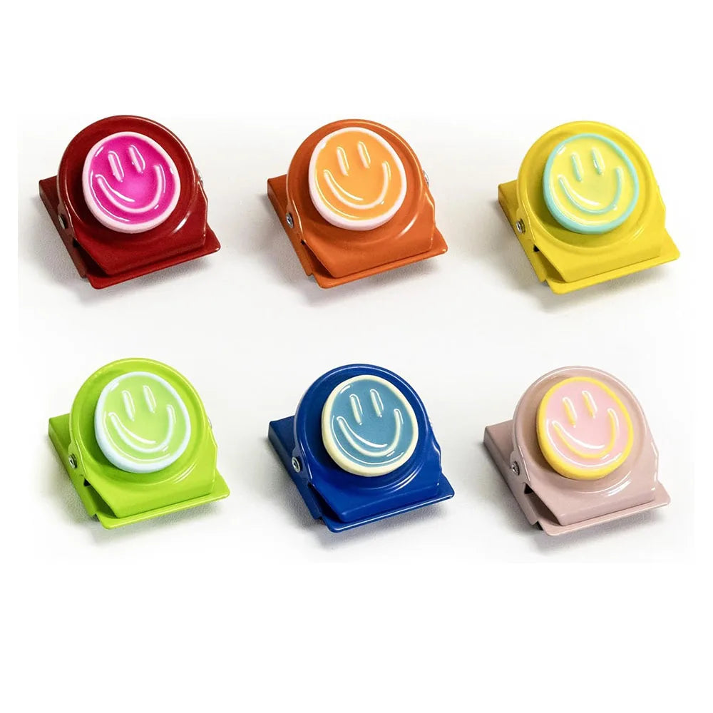Five colorful magnetic clips shaped like smiley faces in various colors are displayed on a white background.