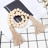 Boho farmhouse tassel bead wall hanging featuring a wreath of light beige wooden beads on a white background.