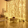 A window decorated with vertical fairy lights creating a warm, glowing curtain effect indoors.