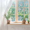 A potted green plant sits on a windowsill next to a window with colorful rainbow suncatcher stickers.
