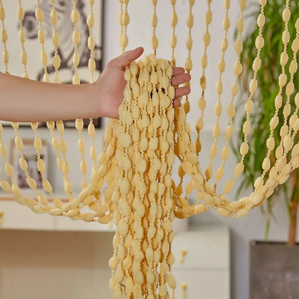 A hand is holding a long, yellow beaded string curtain with tassels, demonstrating the drape and texture.