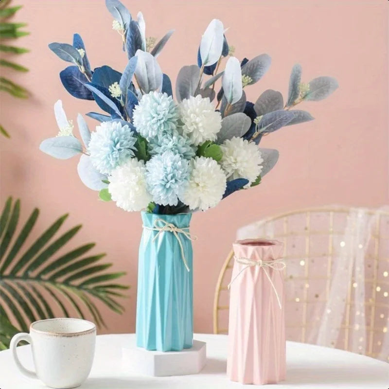 A bouquet of light blue and white flowers in a teal vase on a white table.